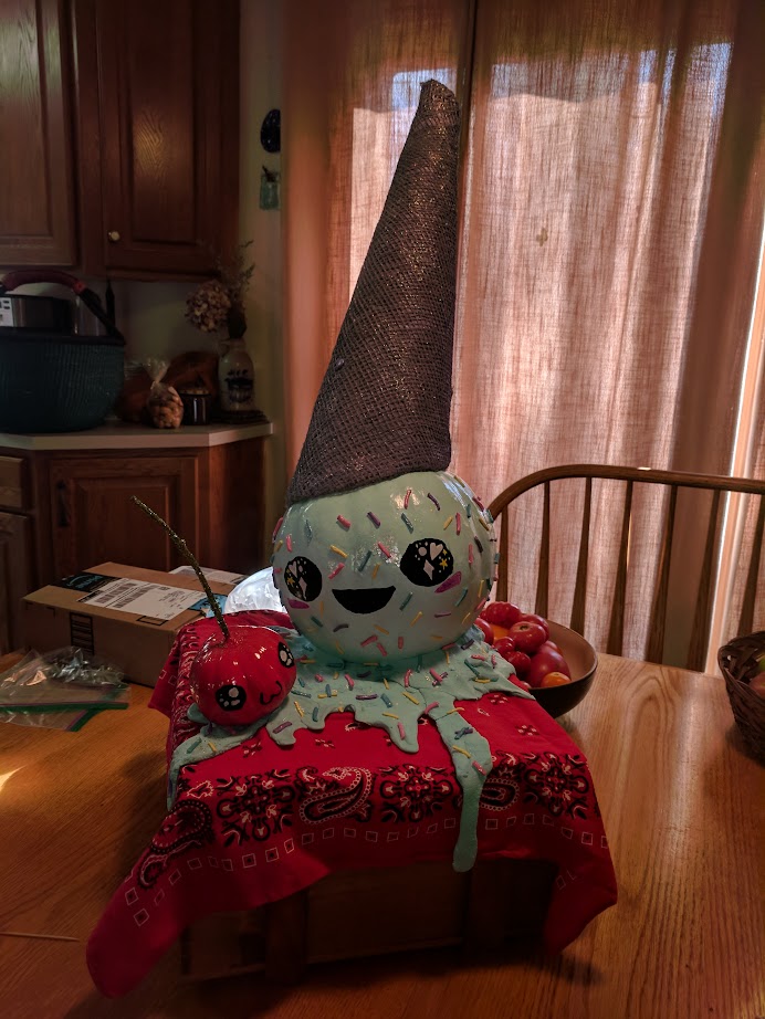 two pumpkins decorated to look like an ice-cream cone and a cherry, they are both smiling despite clearly having been dropped