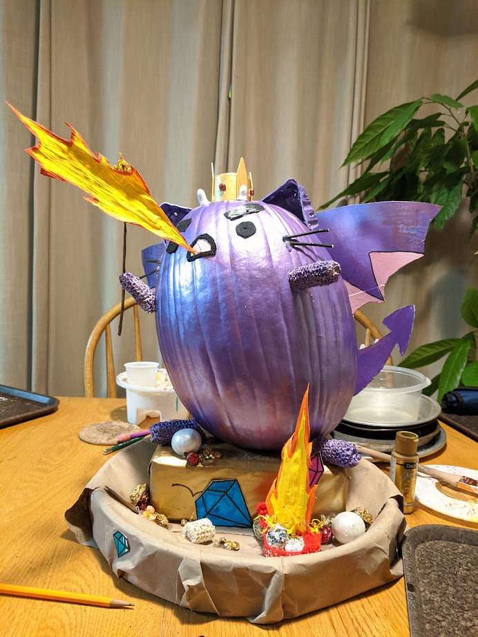 a pumpkin decorated to look like pusheen the cat if pusheen were purple and a dragon and breathing fire